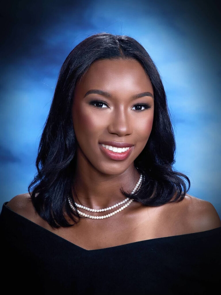 senior portrait with a blue backdrop, black drape, and pearls 