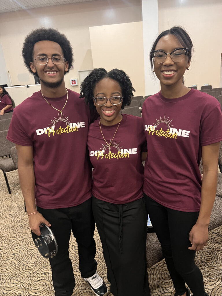 Me and two friends at the Voices of Praise concert wearing burgundy shirts that read "Divine Protection" 