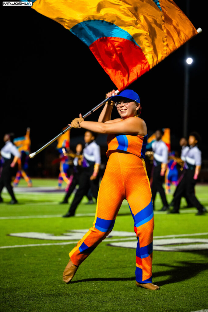 Color guard girl raises and tilts flag to the left behind her head.